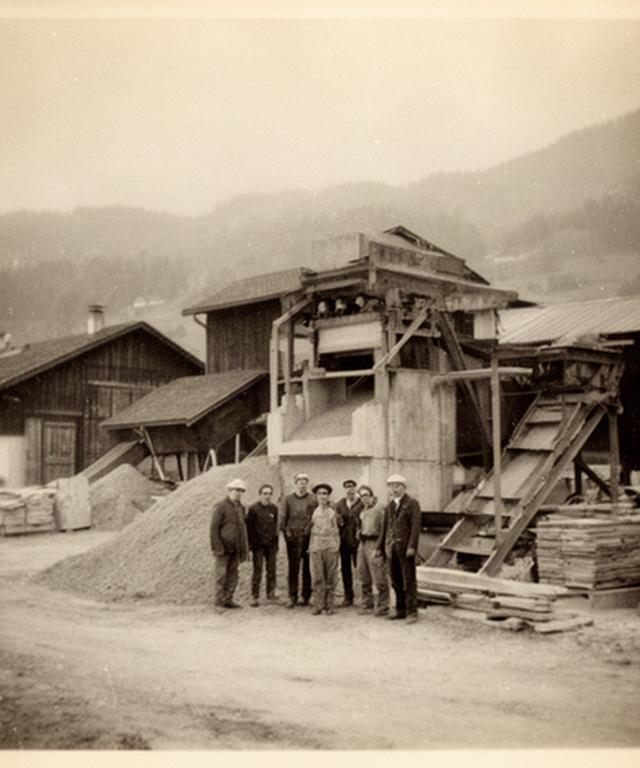 Historische Aufnahme eines frühen Baustoffwerks mit Mitarbeitenden und Materiallager in der Region Nyon